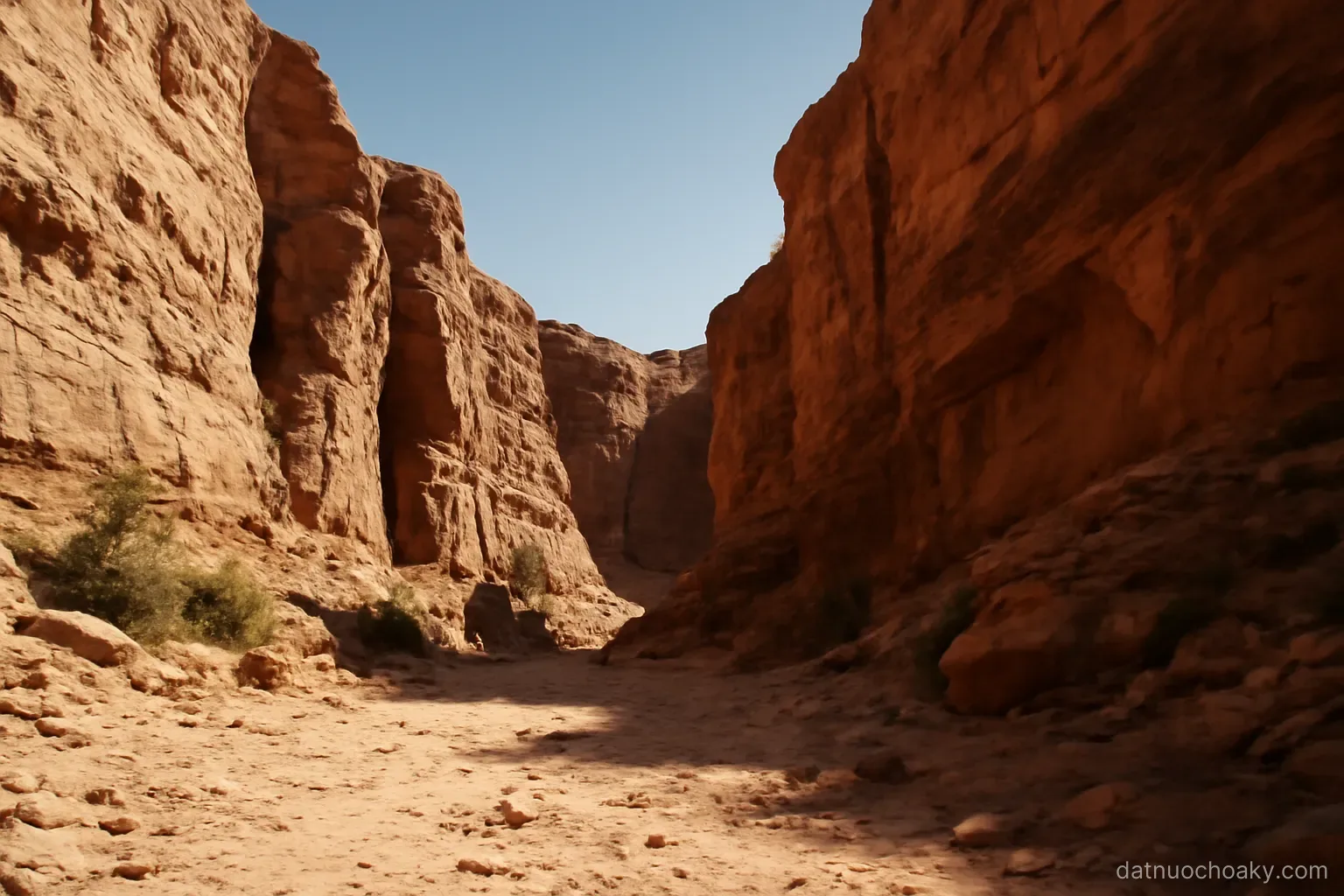 red rock canyon walls with a dry riverbed below, deep shadows, clear sky, no people or structures