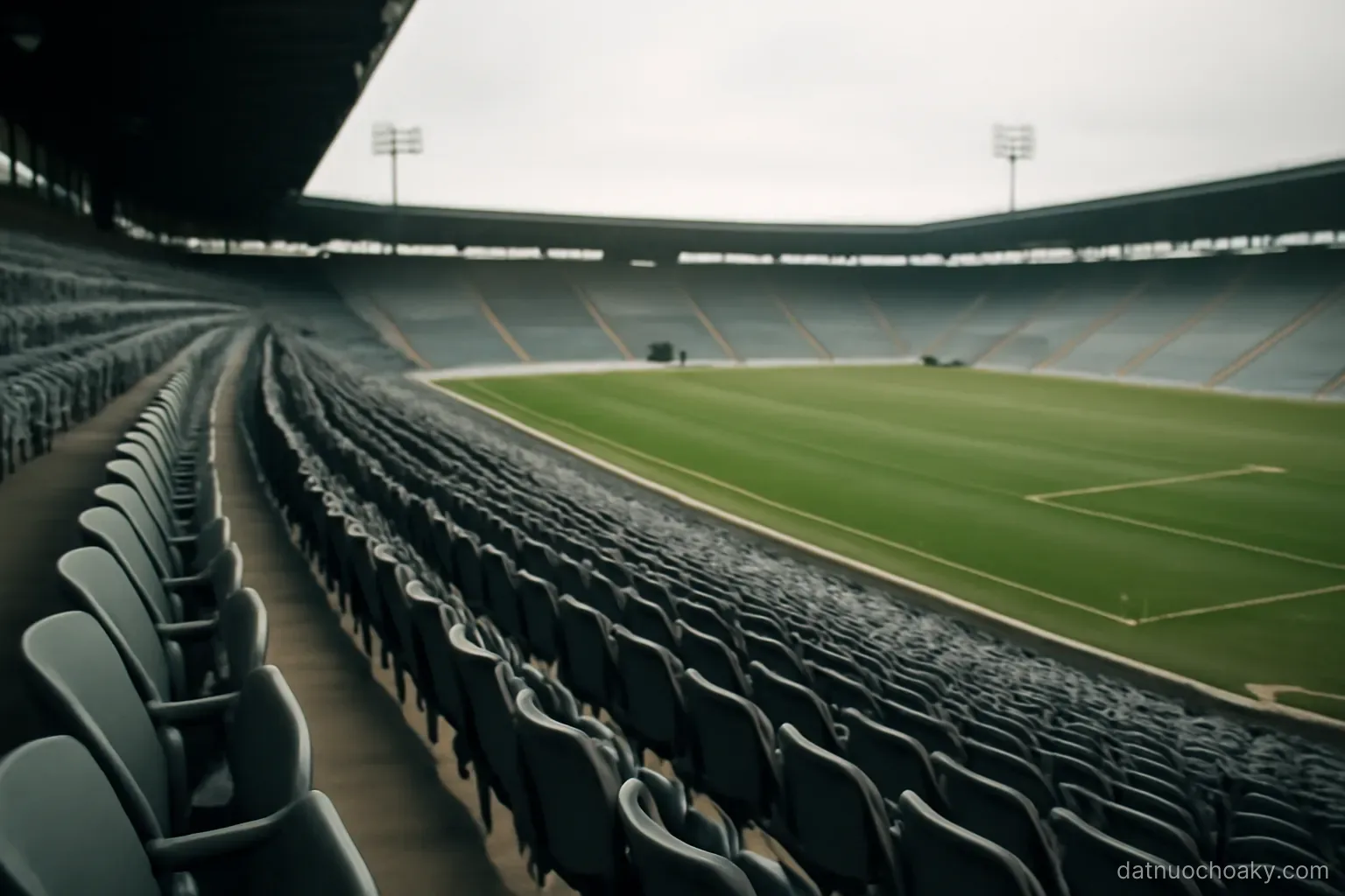 empty stadium seats in long curving rows above a marked field, floodlights off, overcast afternoon
